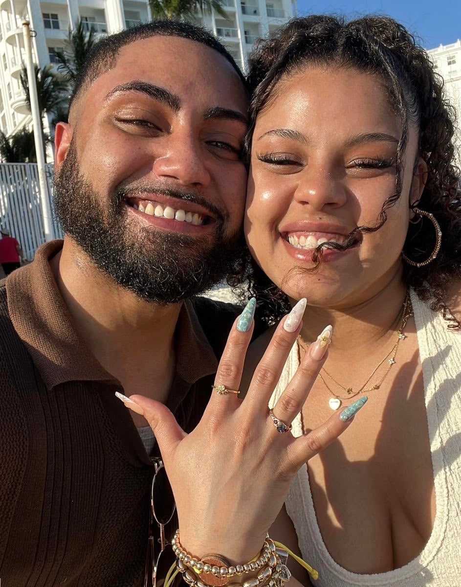 Kenneth and his wife smiling in the sun as she shows her alexandrite and ruby engagement ring