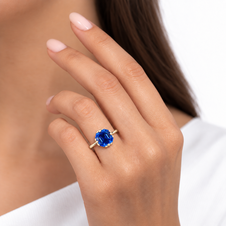 The Verena Asscher blue sapphire ring with leaf prongs in 14K yellow gold, worn on hand