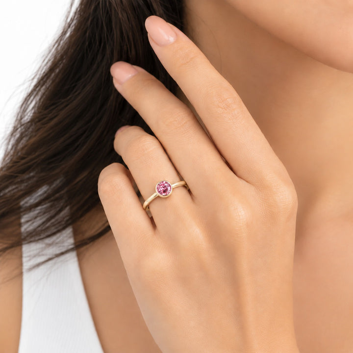 The Lune pink lab sapphire bezel solitaire ring in 14K yellow gold, worn on hand