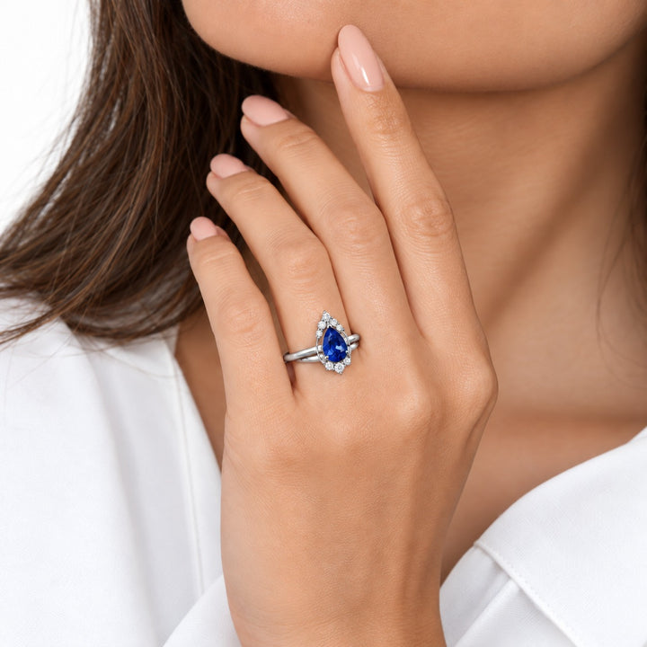 The Teardrop pear blue sapphire ring with diamond halo in platinum, worn on hand