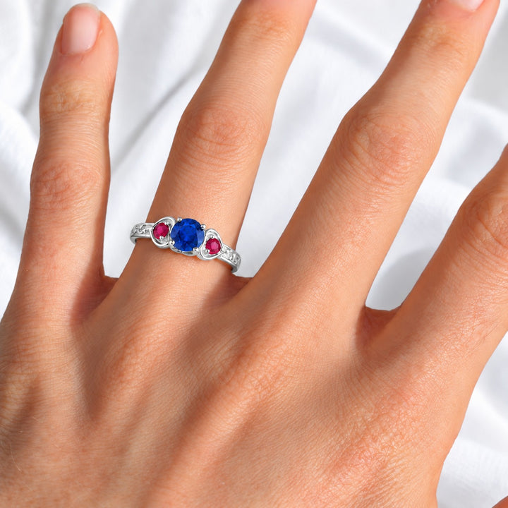 Sapphire and ruby three-stone ring with leaf band in 14K white gold, worn on hand