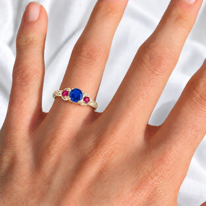 Sapphire and ruby three-stone ring with leaf band in 14K yellow gold, worn on hand